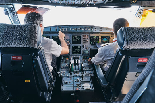 Back view of male pilot and co pilot using instrument panel in cockpit of modern passenger aircraft during flight