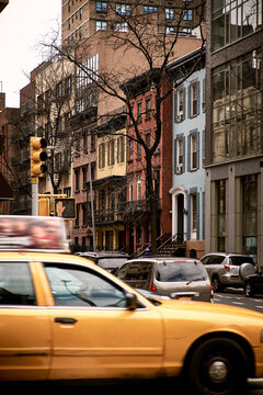 Yellow taxi car driving on crossroad of old city district with typical stone buildings in cloudy spring day in New York City