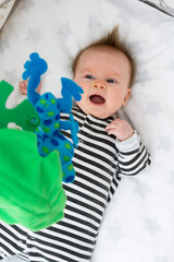 Sleepy cute baby lying in crib or cot bed, looking at crib mobile toys.