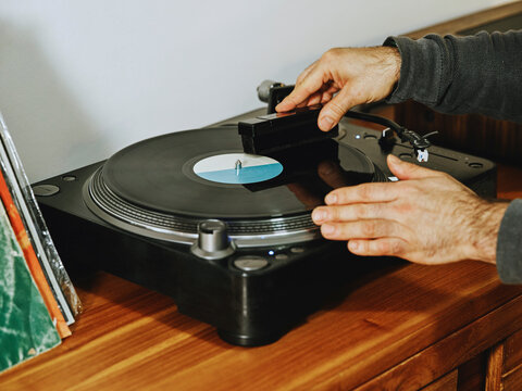 Cropped unrecognizable person setting turntable and enjoying songs on retro vinyl disc while chilling at home