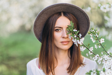 Amazing young woman in hat posing in Blooming tree orchard at spring