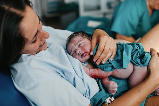 High angle of cheerful adult woman embracing newborn child covered with blood after giving birth in delivery room of contemporary hospital