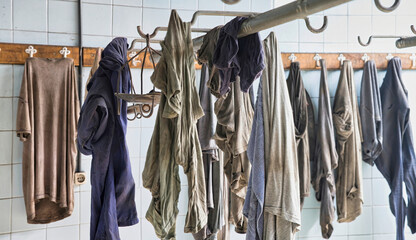 Carelessly scattered dirty miners uniforms hanging on hooks in locker room with white walls tiled in abandoned coal mine
