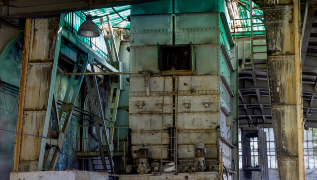 Rusty old tall multi level metal tower with iron staircase leading to small open window in middle of structure surrounded by metal beams in abandoned building of coal mine