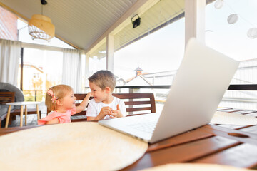 Obraz premium Small smiling kids brother and sister laugh and play laptop, communicate video conference chatting. Spacious cozy home interior.