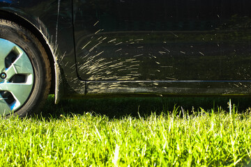 Close-up car wheel on green grass: mud splashes on a black car