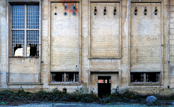 Exterior of abandoned stone industrial building with narrow windows with metal grid and broken glass