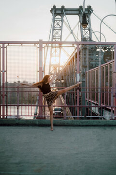 Side view of graceful female dancer in skirt balancing on tiptoe with outstretched arms while practicing choreographic elements on background of cityscape