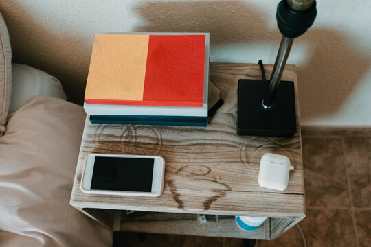 From above notebooks and smartphone in composition with true wireless earphones and lamp on wooden bedside table in cozy bedroom of modern apartment