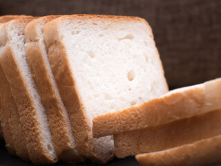 Sliced stack of bread on plate. Background of wooden table. Bread for sandwich. Close up of golden slices in plate.