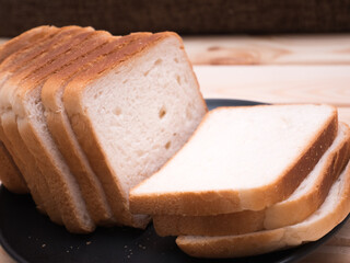 Sliced stack of bread on plate. Background of wooden table. Bread for sandwich. Close up of golden slices in plate.