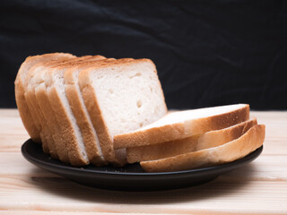 Sliced stack of bread on black plate. Background of wooden table. Bread for sandwich. Golden slices in plate.