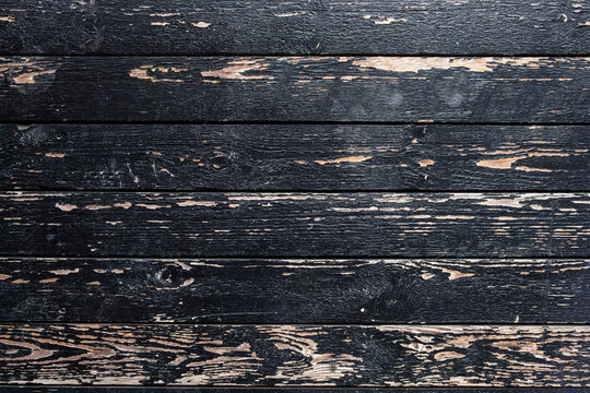 old cracked wooden fence with peeling black paint. horizontal lines. rough surface texture