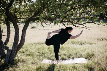 Outdoor yoga. Young overweight woman doing yoga exercise in the meadow. Open air workout, healthy lifestyle, weight loss