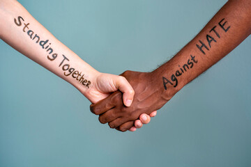 Handshake between black and white human woman and male hands with the message text Standing Together against HATE. Concept of Black Lives Matter protest against racism and police brutality.