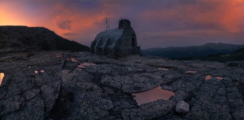 Picturesque landscapes of rocky cliffs with small stone house locating in middle of mountains against cloudy sky at sunset in beautiful evening