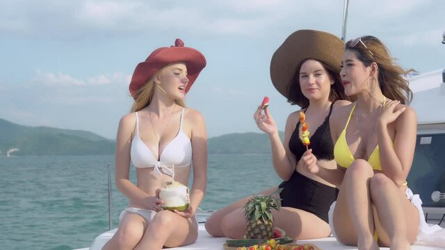 Beautiful group young woman in bikini sexy to travel sitting and eating watermelon and bbq in party in vacation on boat together, happy girl with friend on yacht cruise for relax summer in tropical.