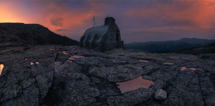 Picturesque landscapes of rocky cliffs with small stone house locating in middle of mountains against cloudy sky at sunset in beautiful evening