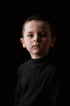 Portrait of thoughtful little boy looking at camera during taking studio shot against black background