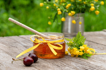 Young honey with a wooden spoon and two cherries on a background of greenery and a bouquet of wild flowers.