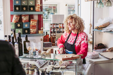Senior man choosing food from freezer while buying wine and cheese from female seller in cozy small store