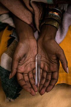 From above of crop anonymous ethnic female in traditional clothes with metal bracelets holding glass tube with incense stick for spiritual ceremony