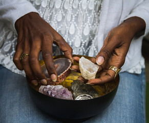 Unrecognizable ethnic female in casual outfit sitting with metal dish with amethyst and agate crystals for rituals