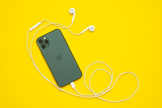 June 05, 2020, Rostov, Russia: midnight green color smartphone iPhone 11 Pro with Apple wired phone headphones of old model on yellow background, top view, copy space for advertising text