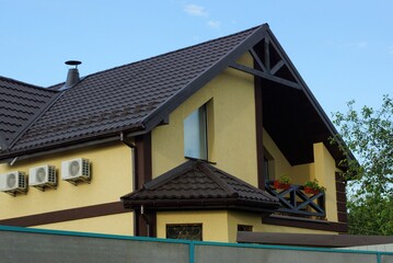 part of a yellow private house with windows and a wooden open balcony under a brown tiled roof against a blue sky