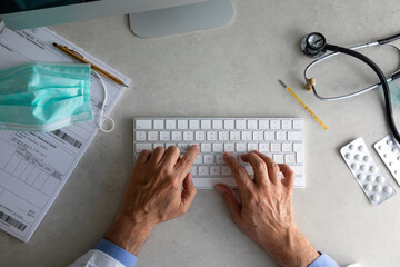 From above of senior male practitioner using wireless keyboard while conducting telemedicine consultation during quarantine