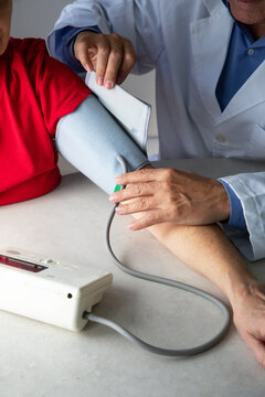 From above of crop physician with stethoscope sitting at table in medical room and measuring blood pressure with tonometer while working in hospital during coronavirus outbreak