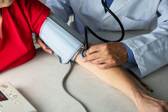 From above of crop physician with stethoscope sitting at table in medical room and measuring blood pressure with tonometer while working in hospital during coronavirus outbreak