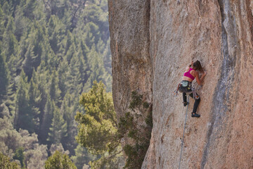From above active female alpinist in sportswear with rope and safety equipment ascending rocky slope of high mountain on sunny day