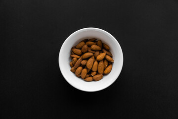 Almonds in a small plate on a black table. Almond is a healthy vegetarian protein nutritious food. Natural nuts snacks.
