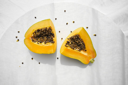 Top view of halves of fresh healthy papaya with seeds placed on white table