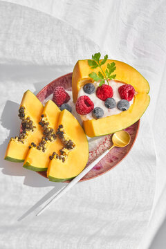 From above pieces of ripe papaya with yoghurt and fresh berries placed near spoon on plate on white background