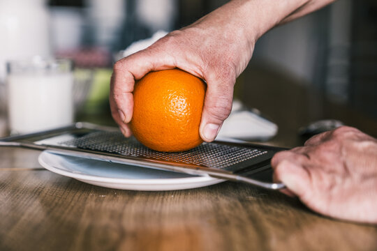 Side view of crop anonymous woman removing orange zest with grater while preparing aromatic pastry in home kitchen