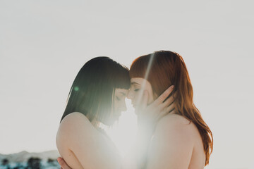 Sensual tender young women in love with bare shoulders embracing and kissing while standing in back lit in snowy field