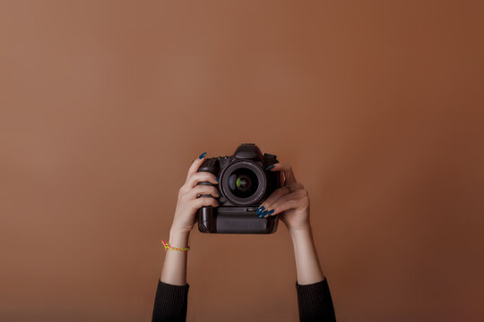 Photographer girl shooting images. Woman hands holding camera taking photos. Vivid brown background. World photography day. Studio photography. Space for text. Top view, minimalism