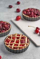 vegan tartlets with cherries and strawberries on a light gray background and marble board