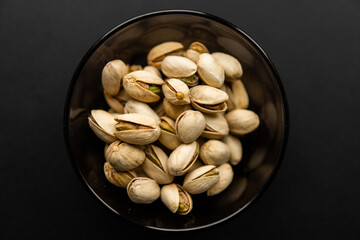 Pistachios in a small plate on a black table. Pistachio is a healthy vegetarian protein nutritious food. Natural nuts snacks.