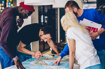 Cheerful group of multicultural students searching right route on map 