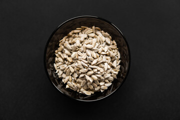 Sunflower seeds in a small plate on the black table. Healthy vegetarian protein nutritious food. Sunflower seed on rustic old wood.