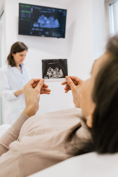 Unrecognizable pregnant female inspecting sonogram picture while lying on bed in ward of modern fertility clinic