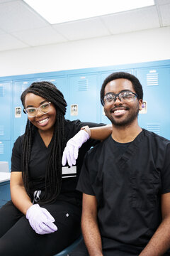 Happy African American woman with braids and black bearded man smiling and looking at camera while creating dentures in modern laboratory