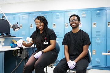 Happy African American woman with braids and black bearded man smiling and looking at camera while creating dentures in modern laboratory