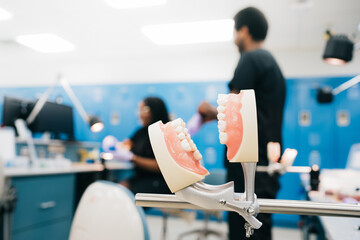 False teeth attached to metal occludator on blurred background of modern orthodontic lab and ethnic staff