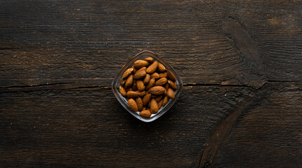 Almonds in a small plate on a vintage wooden table. Almond is a healthy vegetarian protein nutritious food. Natural nuts snacks.