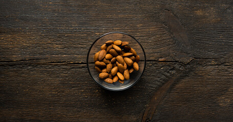 Fototapeta na wymiar Almonds in a small plate on a vintage wooden table. Almond is a healthy vegetarian protein nutritious food. Natural nuts snacks.