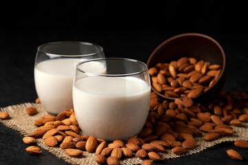 almond milk without sugar and lactose in glass with sprinkled nuts, vegetarian milk drink on a dark black table